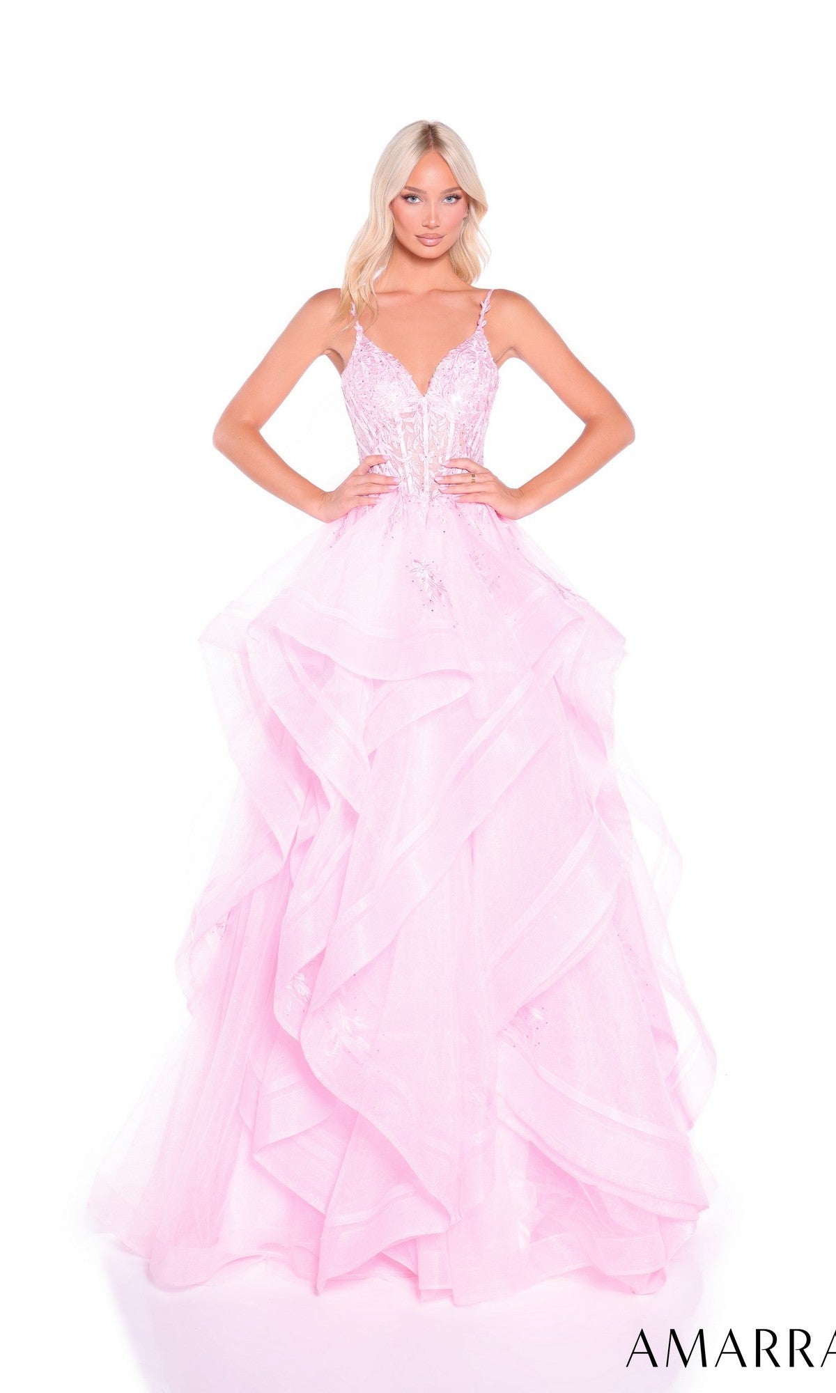 A woman stands with hands on hips wearing the Amarra 89511 long prom dress—a light pink gown with a fitted, sparkly lace corset bodice, thin straps, and a glitter tulle skirt.
